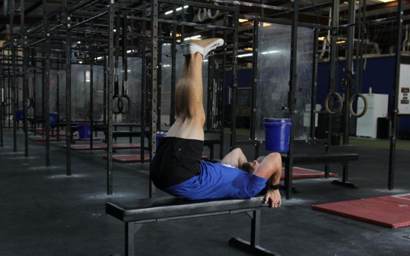 Fit man doing a lying leg raise on the bench in the gym.