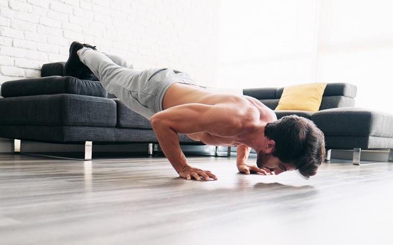 Shirtless brunette man doing feet elevated push up's at home