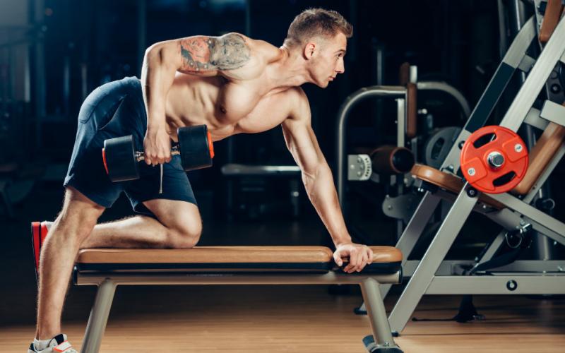 Man doing single arm dumbbell row on flat bench in gym.