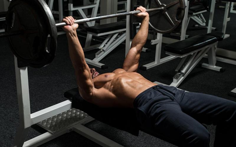 Muscular man doing a barbell bench press in the gym.
