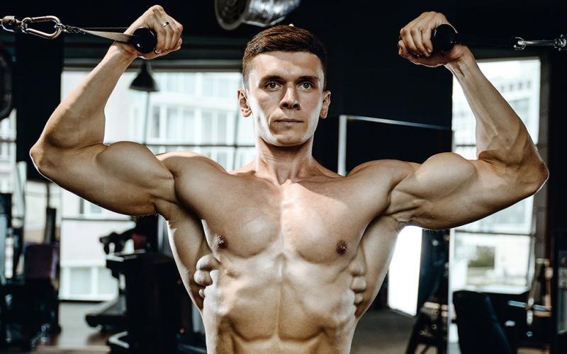 Muscular man shirtless doing bicep curls in the gym