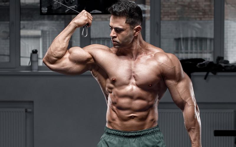 Frontal shot of muscular shirtless man using the cables at the gym