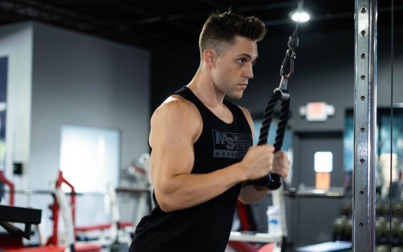 Muscular man wearing a black tank top doing cable tricep push downs.