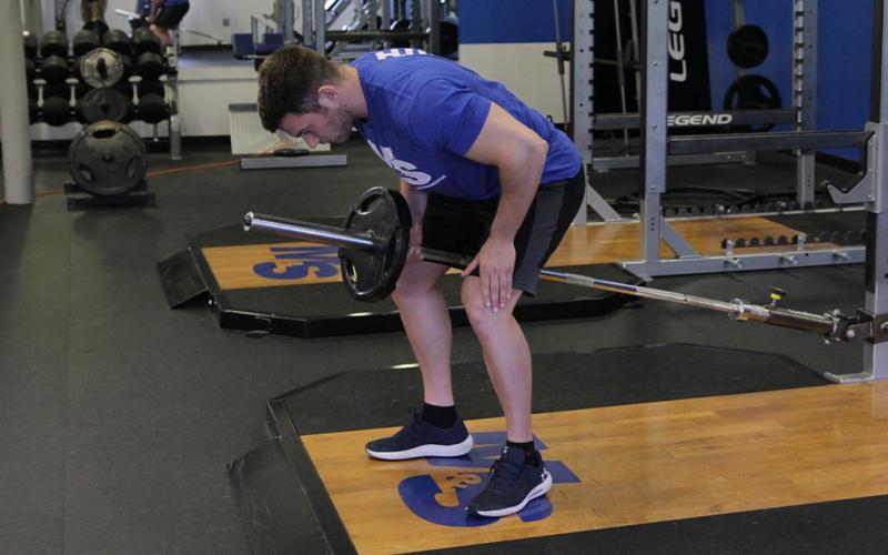 Fit man doing one-arm bent over barbell row in the gym.