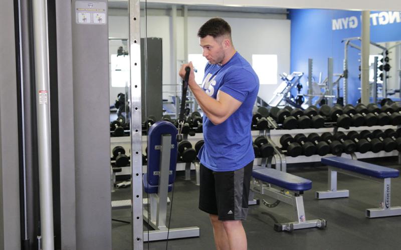Fit man doing a one-arm cable curl in the gym.