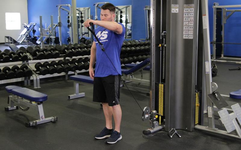 Fit man doing a one-arm cable front raise in the gym.