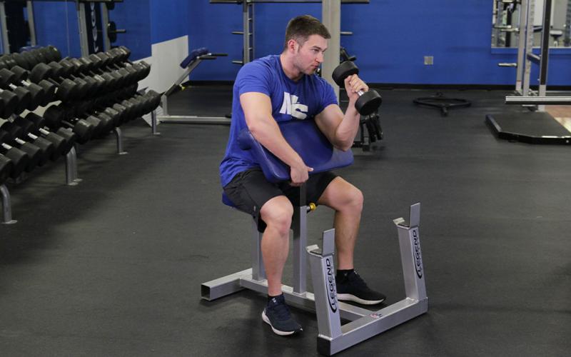 Fit man doing a one-arm dumbbell hammer preacher curl in the gym.