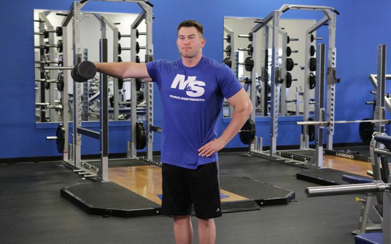 Fit man doing a one-arm dumbbell lateral raise in the gym.