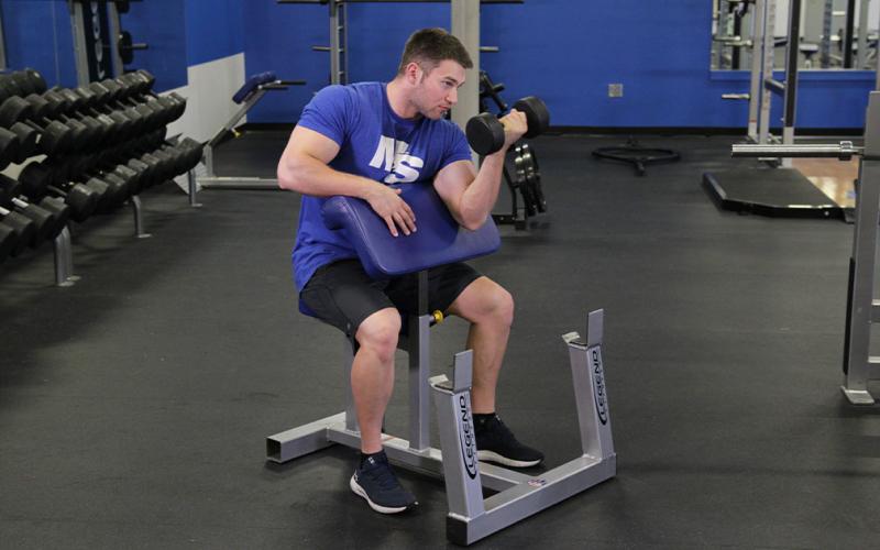 Fit man doing a one-arm dumbbell preacher curl.
