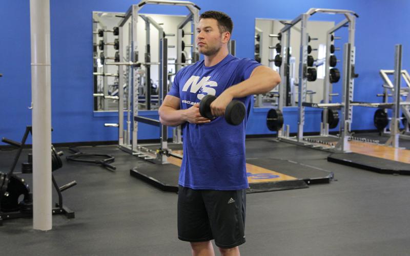 Fit man doing a one-arm dumbbell upright row in the gym.