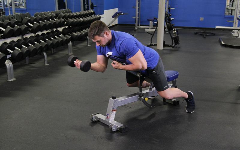 Fit man doing a one-arm prone incline dumbbell curl in the gym.