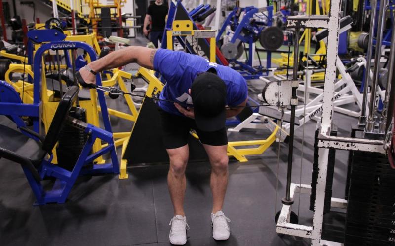 Fit man doing a One-Arm Bent-Over Cable Reverse Fly in the gym