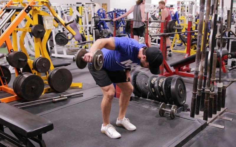 Fit man doing a one-arm dumbbell rear delt fly in the gym.