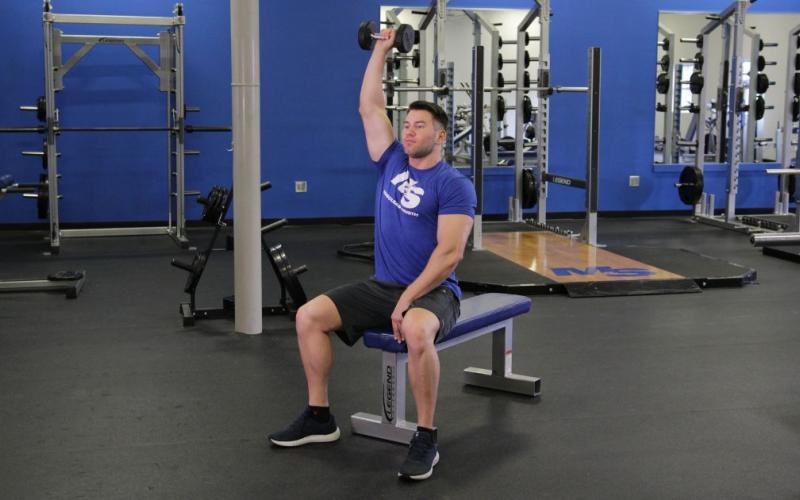 Fit man doing a one-arm seated dumbbell shoulder press in the gym.
