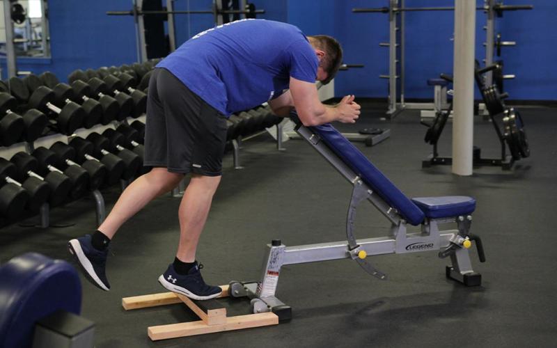 Fit man doing a one-leg donkey calf raise in the gym.