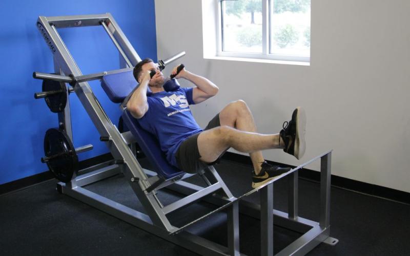 Fit man doing a One-Leg Hack Squat in the gym.