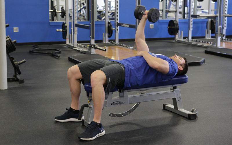 Fit man doing a one-arm dumbbell bench press in the gym.
