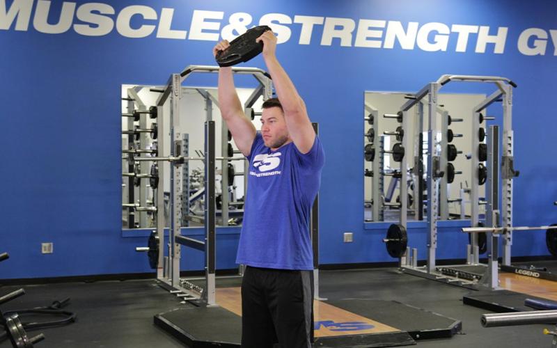 Fit man doing overhead front raise with weight plate in the gym.
