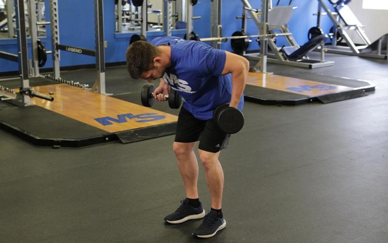 Fit man doing a palm rotational row with dumbbells in the gym.