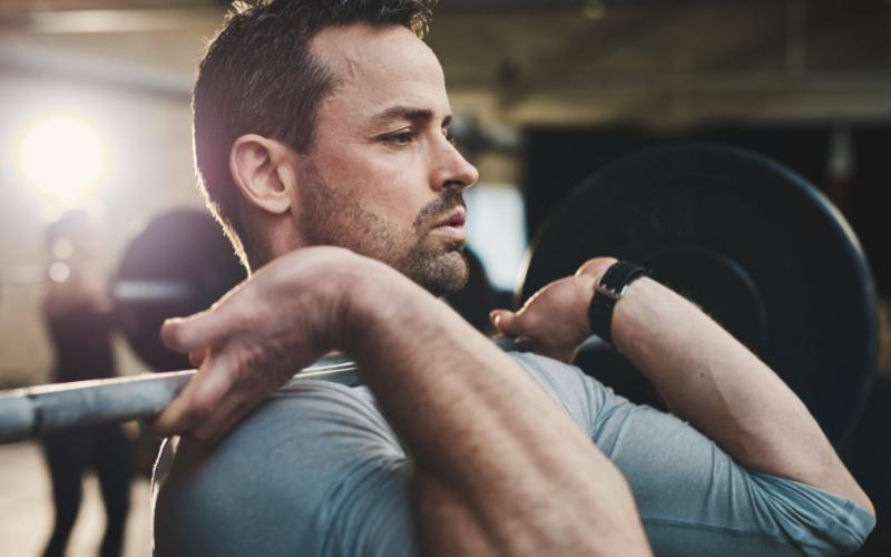 Close up of man holding barbell in front rack position.