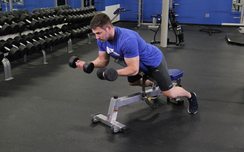 Fit man doing a prone incline dumbbell curl in the gym.