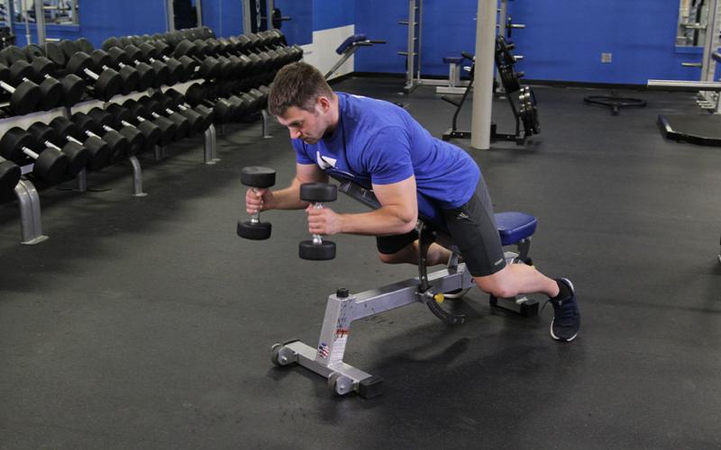 Fit man doing a prone incline hammer curl in the gym.