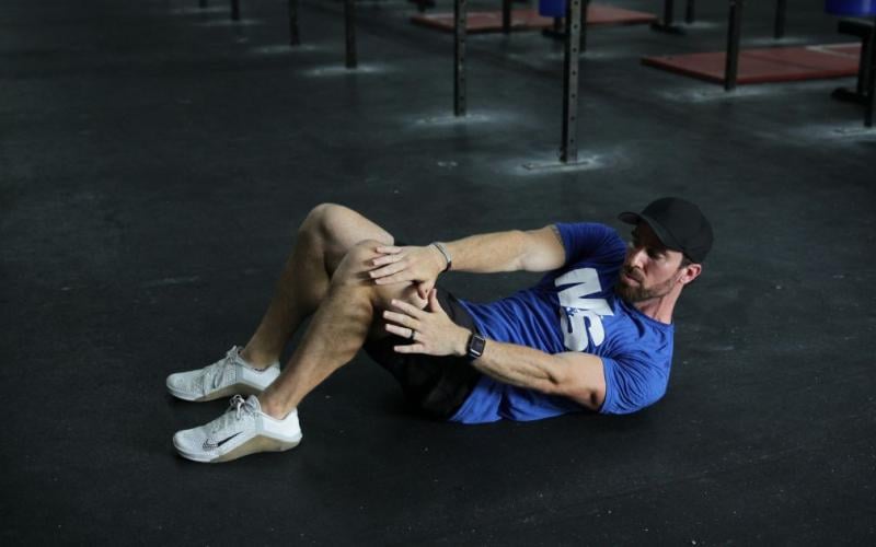 Fit man doing reach and catches on the floor in the gym.