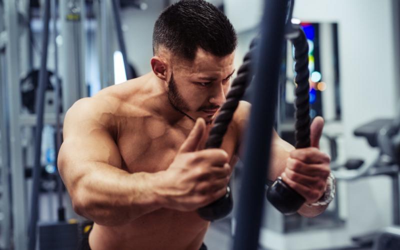 Man doing cable rope tricep pushdowns in gym.