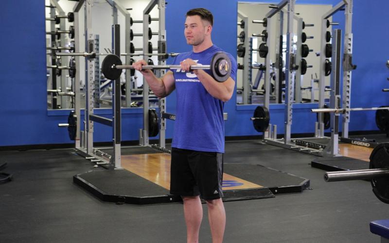Fit man doing a reverse grip barbell curl in the gym.