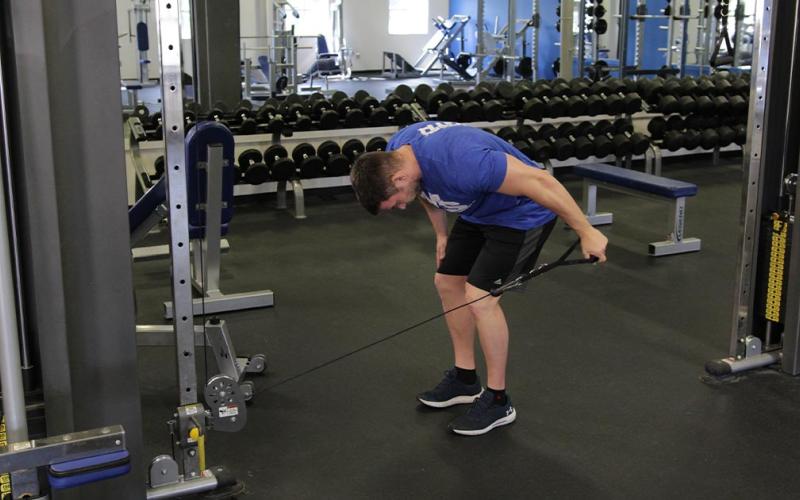 Fit man doing a reverse grip cable tricep kickback in the gym.