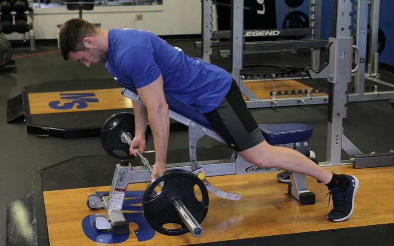 Fit man doing a reverse grip incline bench barbell row in the gym.