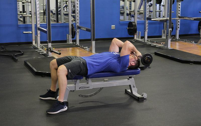 Fit man doing a reverse grip skull crusher in the gym.