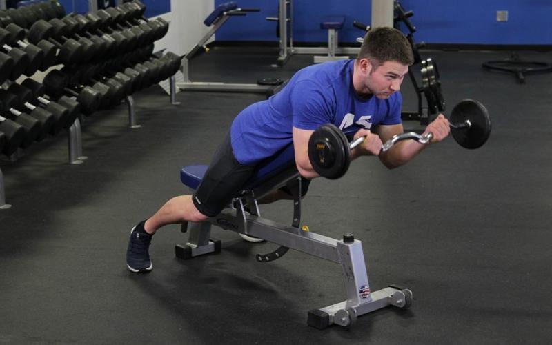 Fit man doing a lying incline bench barbell curl in the gym.