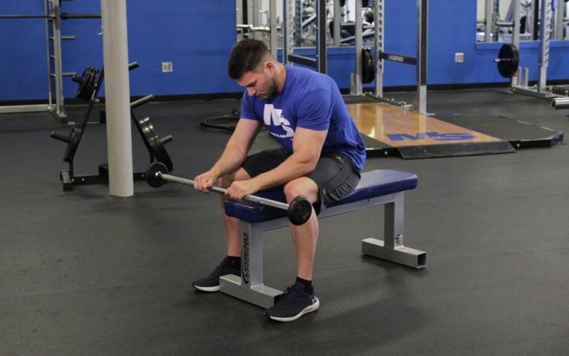 Fit man doing a Reverse Grip Barbell Wrist Curl in the gym.