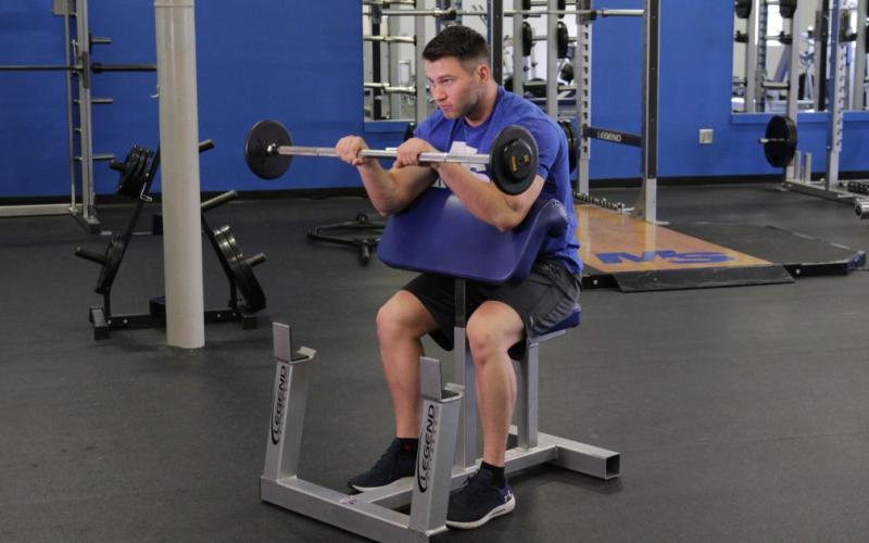 Fit man doing a Reverse Grip Preacher Curl in the gym.