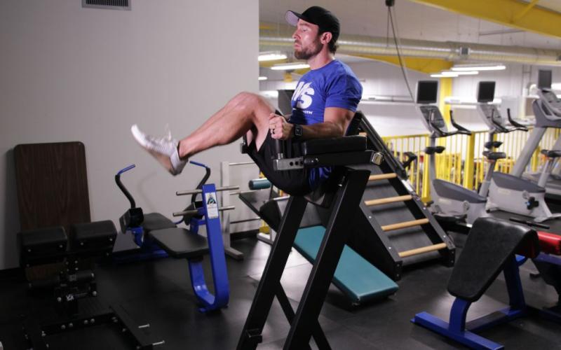Fit man doing a roman chair knee raise in the gym.