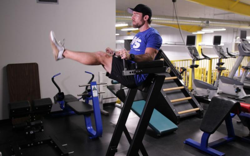 Fit man doing a Roman Chair Leg Raise in the gym.