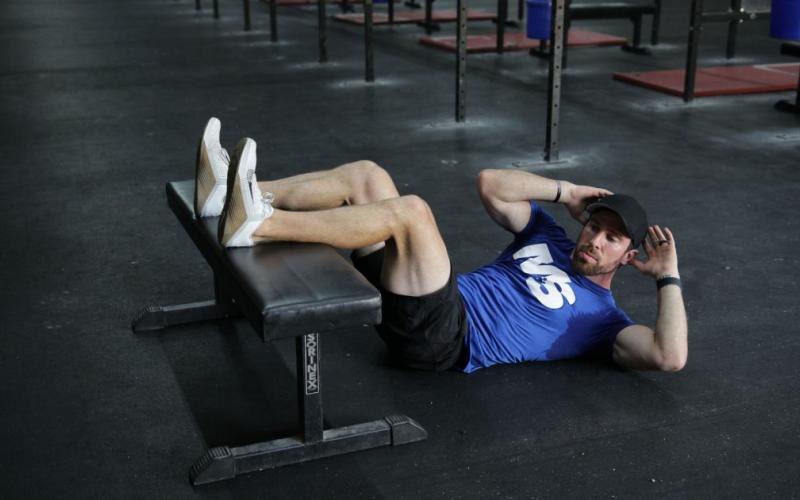 Fit man doing rotating crunches on the floor with his legs on the bench.