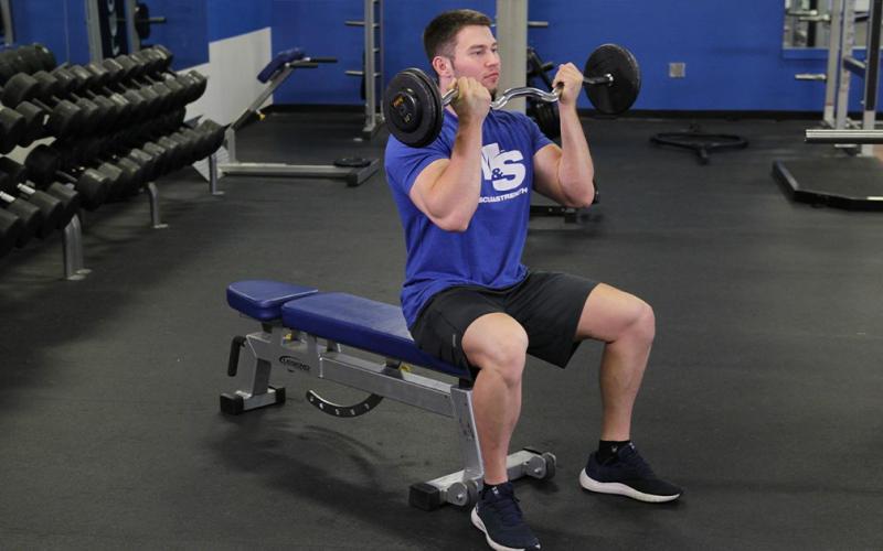 Fit man doing a seated barbell curl in the gym.