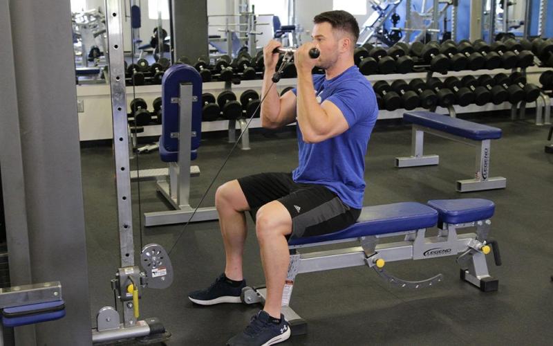 Fit man doing a seated cable curl in the gym.