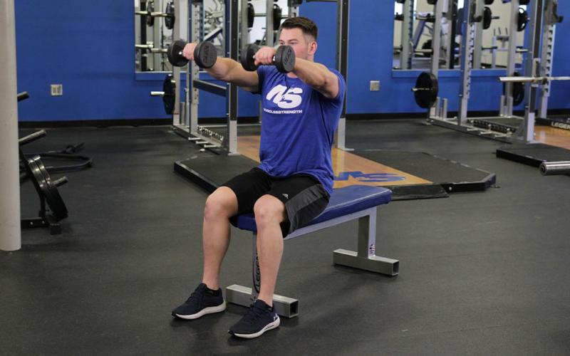 Fit man doing a seated dumbbell front raise in the gym.