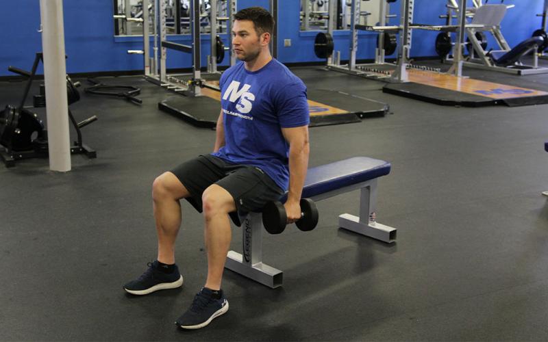 Fit man doing a seated dumbbell shrug in the gym.