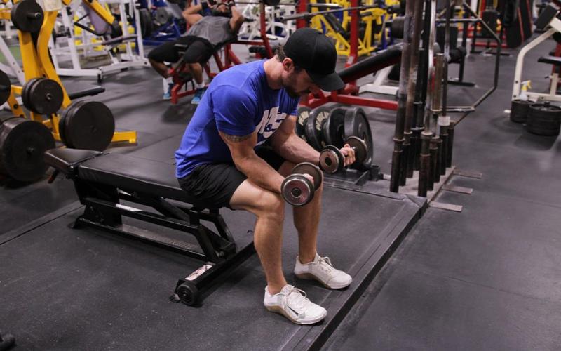 Fit man doing a seated dumbbell wrist curl in the gym.