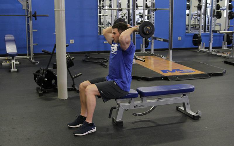Fit man doing a seated french press in the gym.