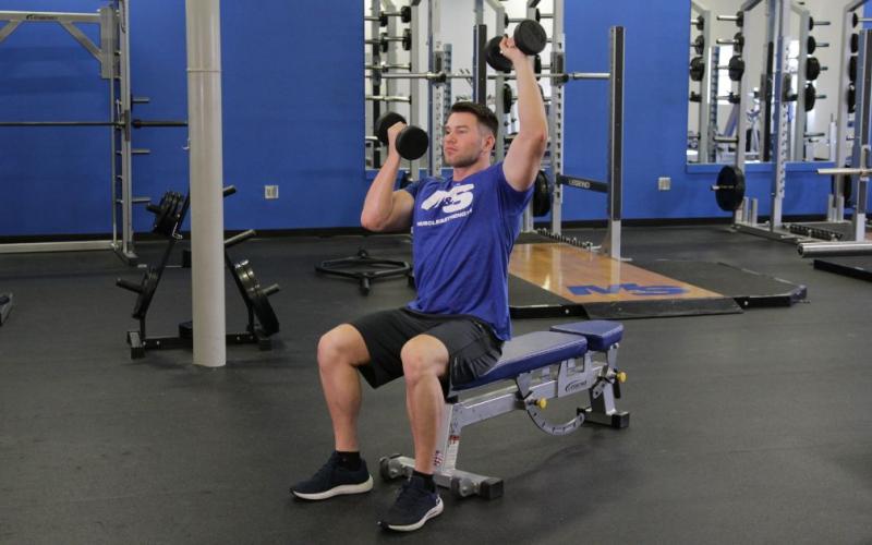 Fit man doing a Seated Alternating Arnold Press in the gym.