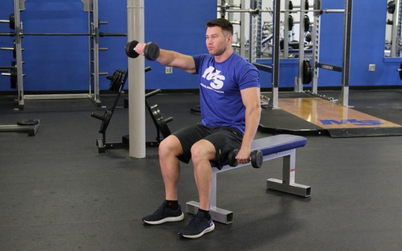 Fit man doing a Seated Alternating Dumbbell Front Raise in the gym.