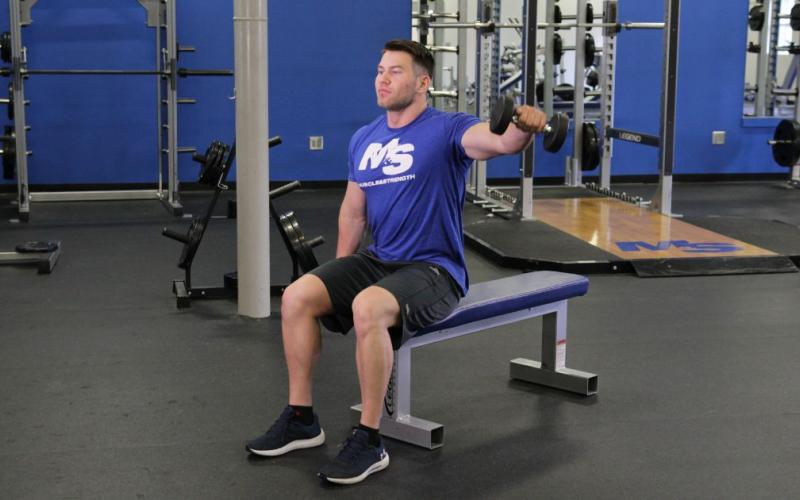 Fit man doing a Seated Alternating Dumbbell Lateral Raise in the gym.