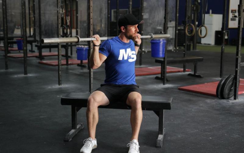 Fit man doing a Seated Barbell Twist in the gym.