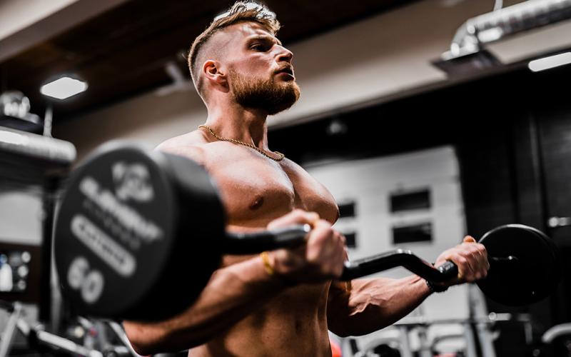 Shirtless muscular man doing bicep curls in the gym
