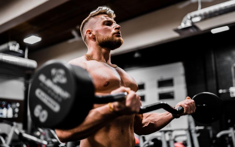 Shirtless muscular man doing bicep curls in the gym.